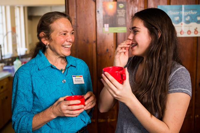 A woman and a teen girl laugh together as they sip mugs of organic coffee.