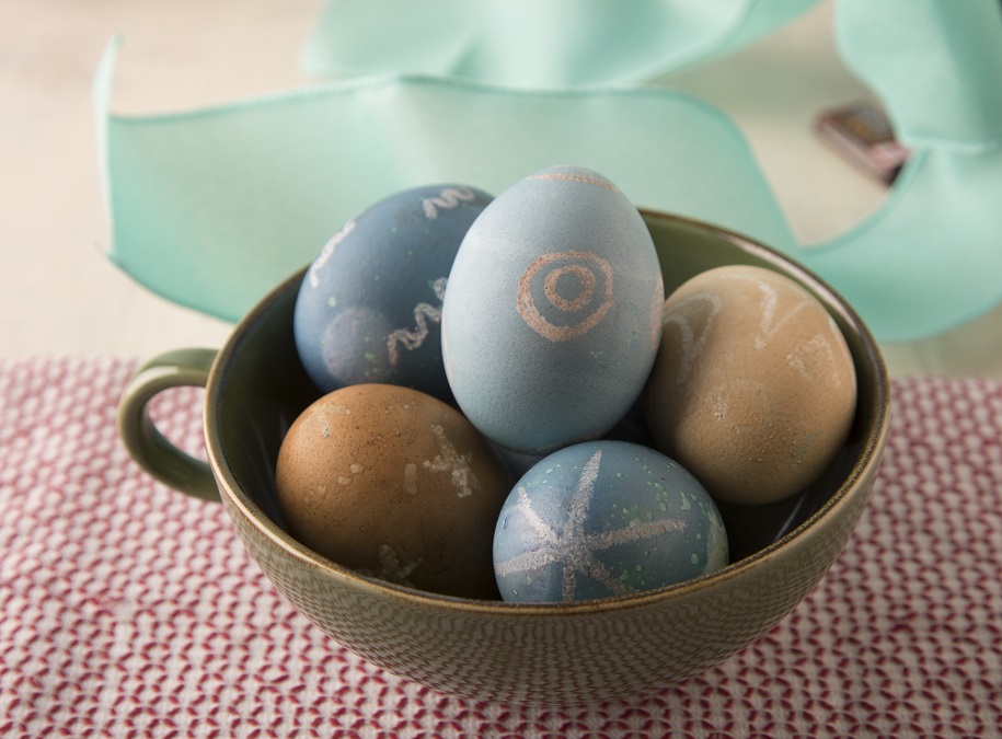 Five natural dyed eggs for Easter in brown and blue sit in an oversized coffee cup.