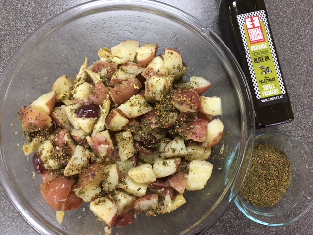 A glass bowl of mayo-free potato salad with a bottle of fair trade olive oil and za'atar spices.