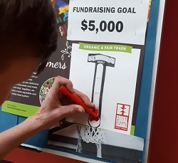 Image is of a student coloring in thermometer on a fundraising goal board.