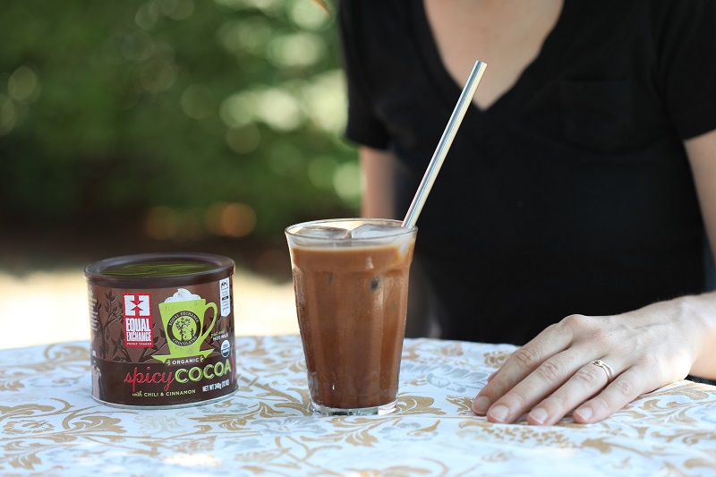 A mocha made with organic spicy hot cocoa sits in a sweating glass, accompanied by a straw and ready to drink.