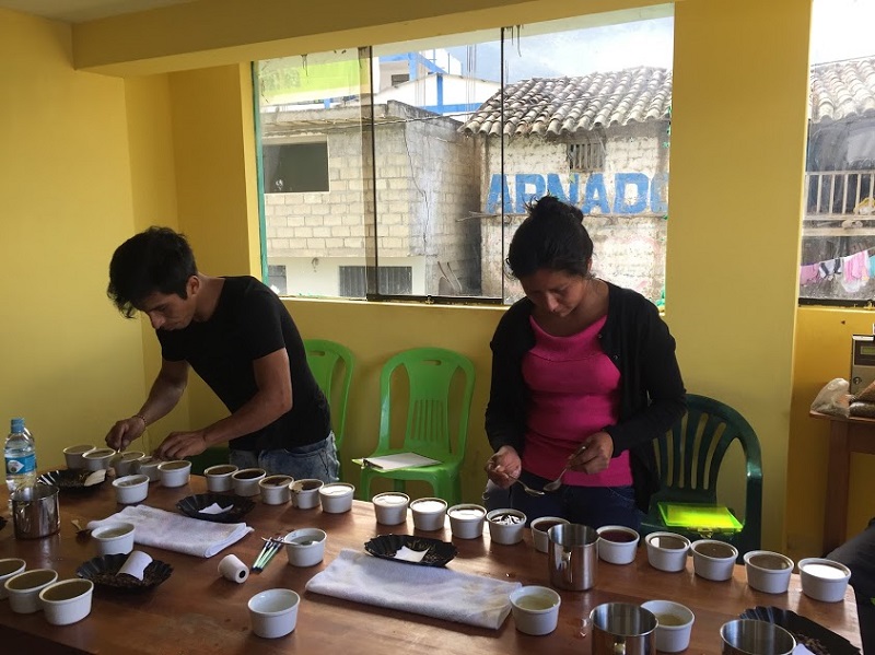A man and a woman sip from tiny cups of organic coffee set along a table