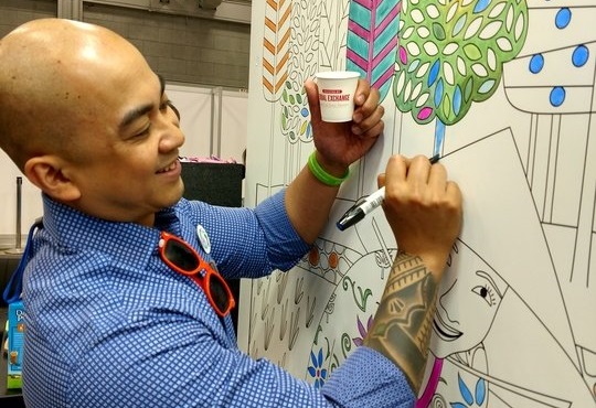 Image shows a smiling man participating in an interactive art project while holding an Equal Exchange coffee cup.