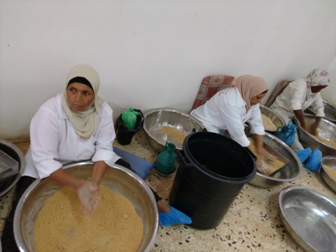 Three seated women bend over large bowls of grain