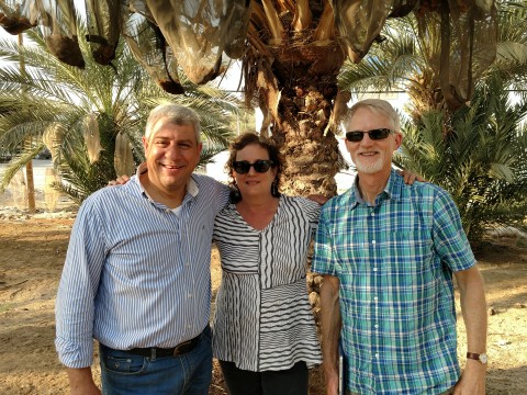 Three people smile in front of a palm tree