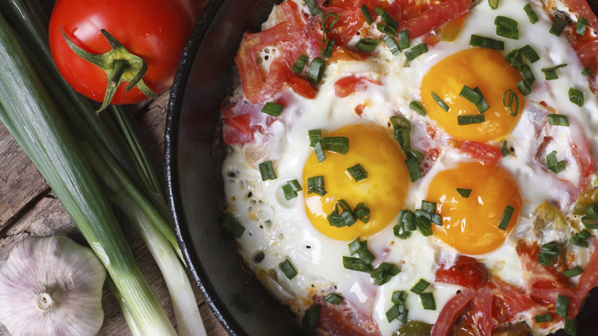 Fried eggs in a skillet with tomatoes and garlic