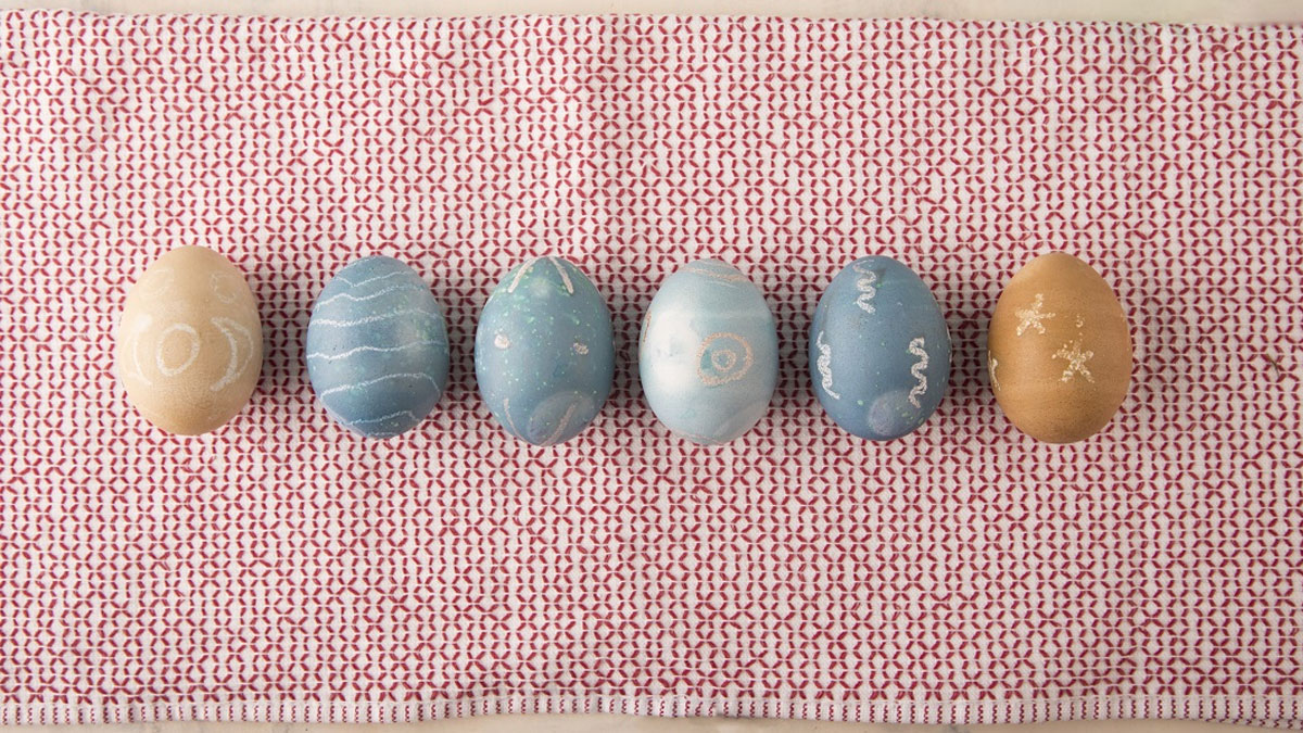 six naturally dyed Easter eggs lined up on a festive red-and-white cloth.