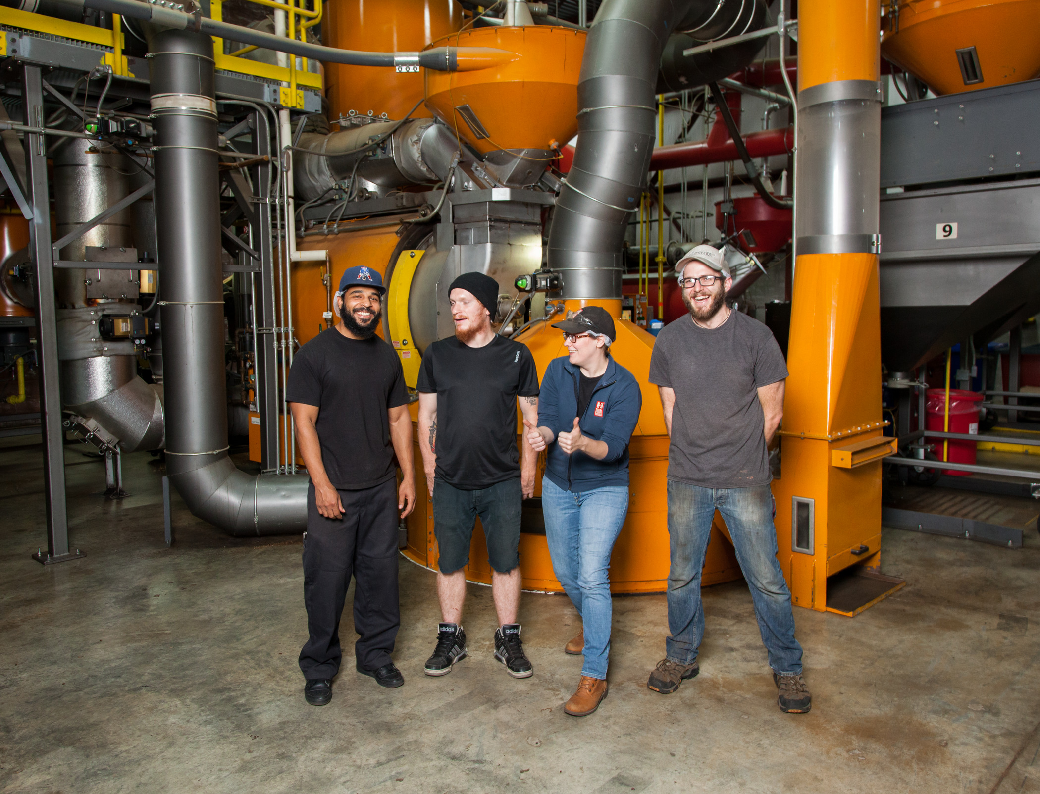 Four men and women stand in front of coffee roasing equipment