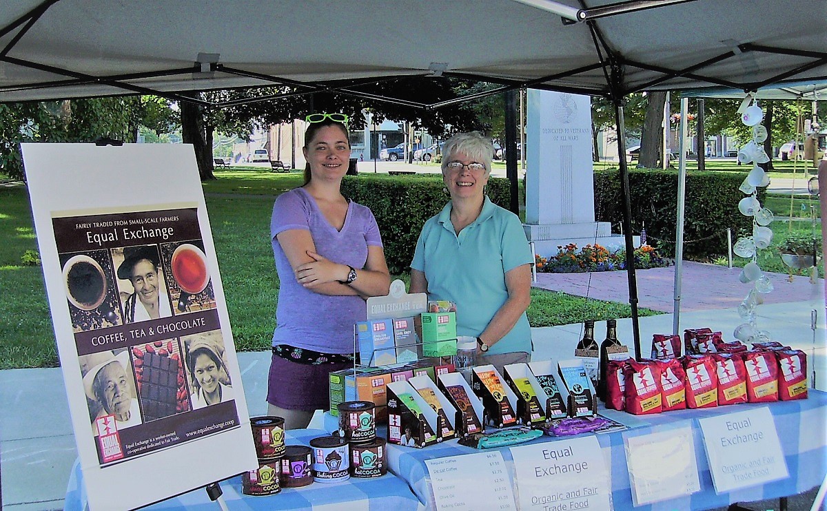 Two women smile at an outdoor table displaying packaged fair trade coffee and chocolate.