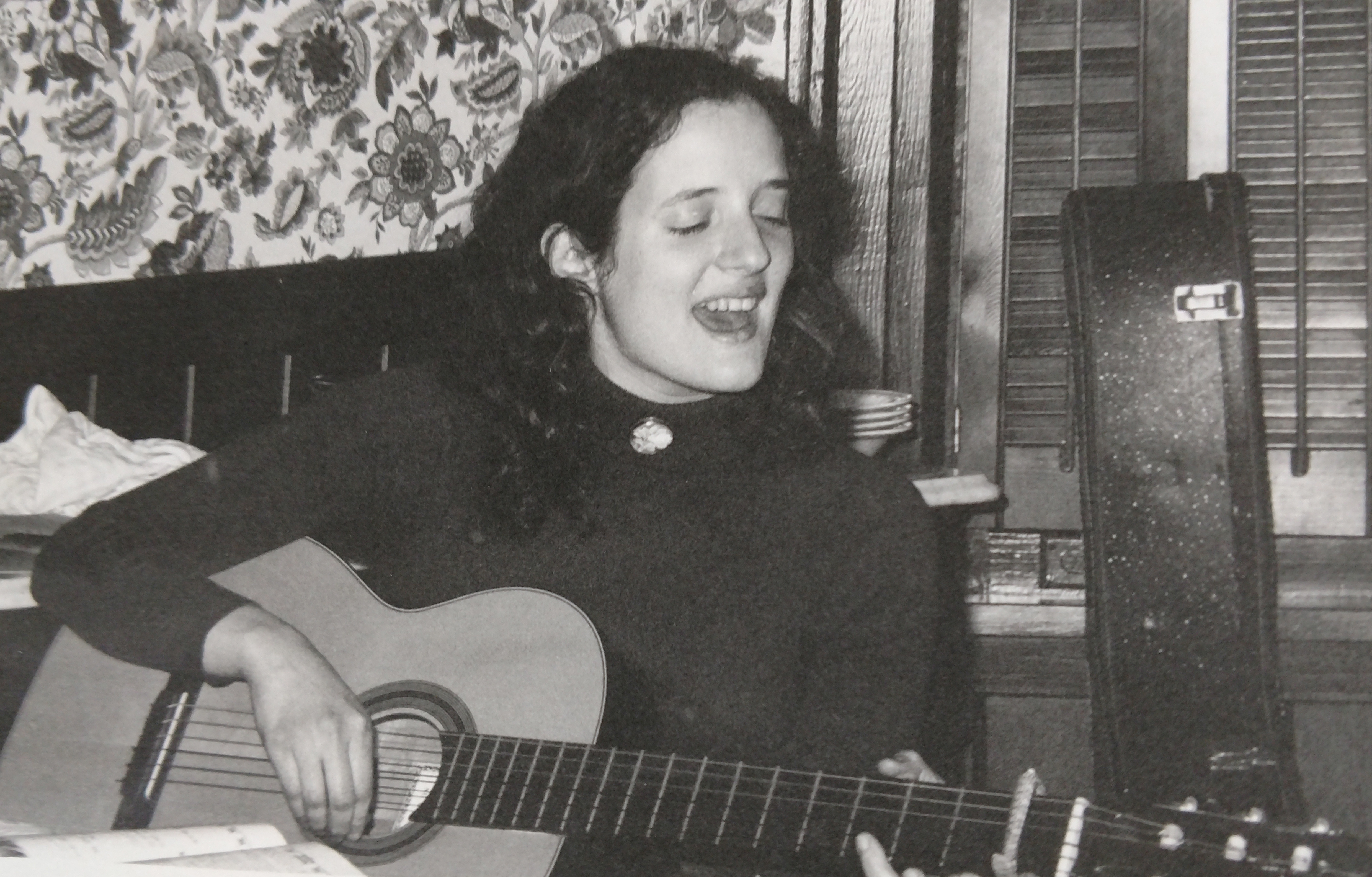 A vintage picture of a woman singing and strumming an acoustic guitar