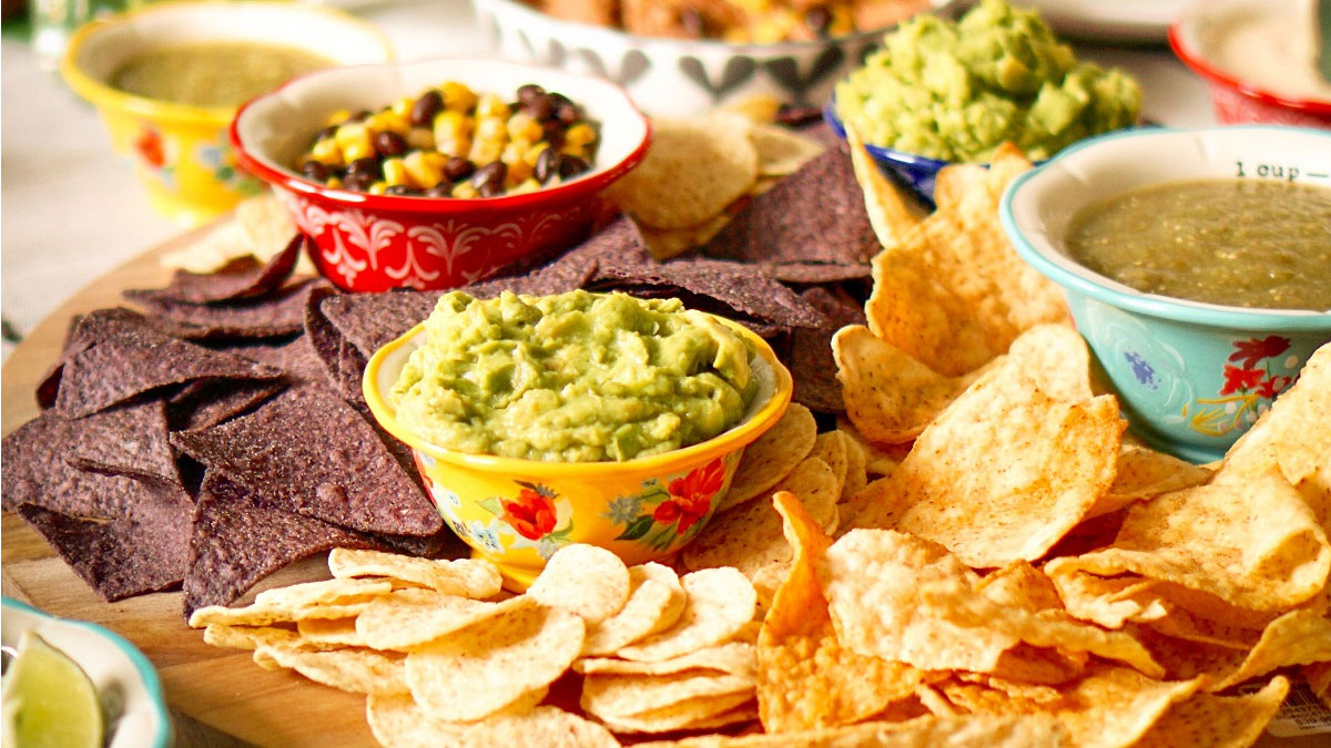Bowls of food, including fresh guacamole and corn chips, crowd a table