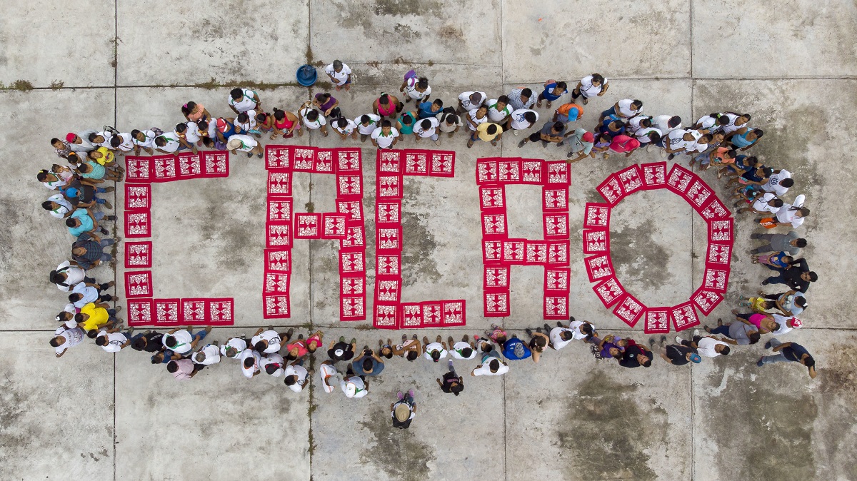 An aerial view of red bandanas spelling out "cacao" with farmers gathered around.