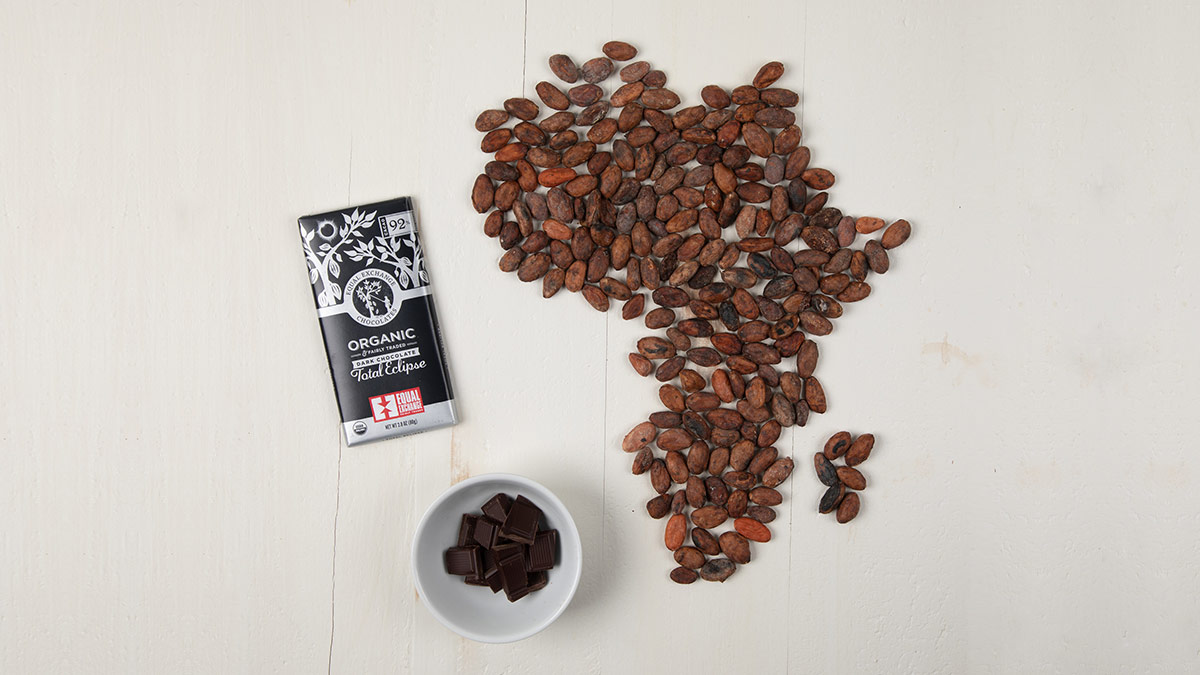 Cacao beans on a table form the shape of Africa, along with a bar of Total Eclipse chocolate