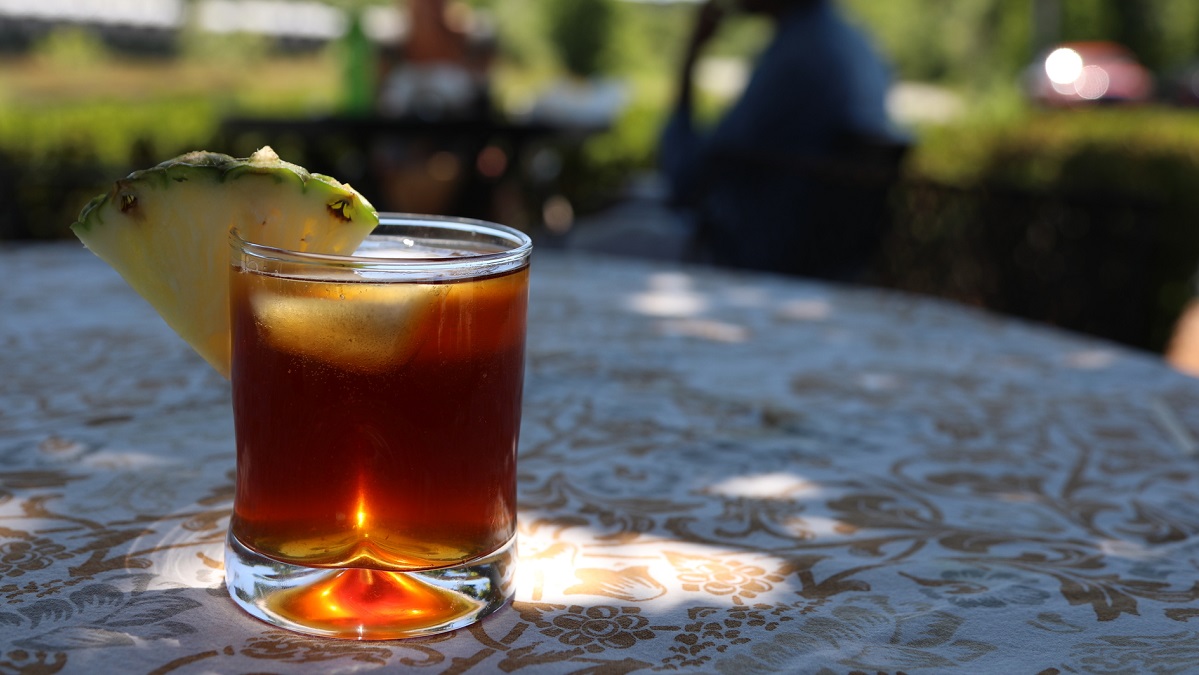A coffee cocktail garnished with pineapple sits on a table in the sun.