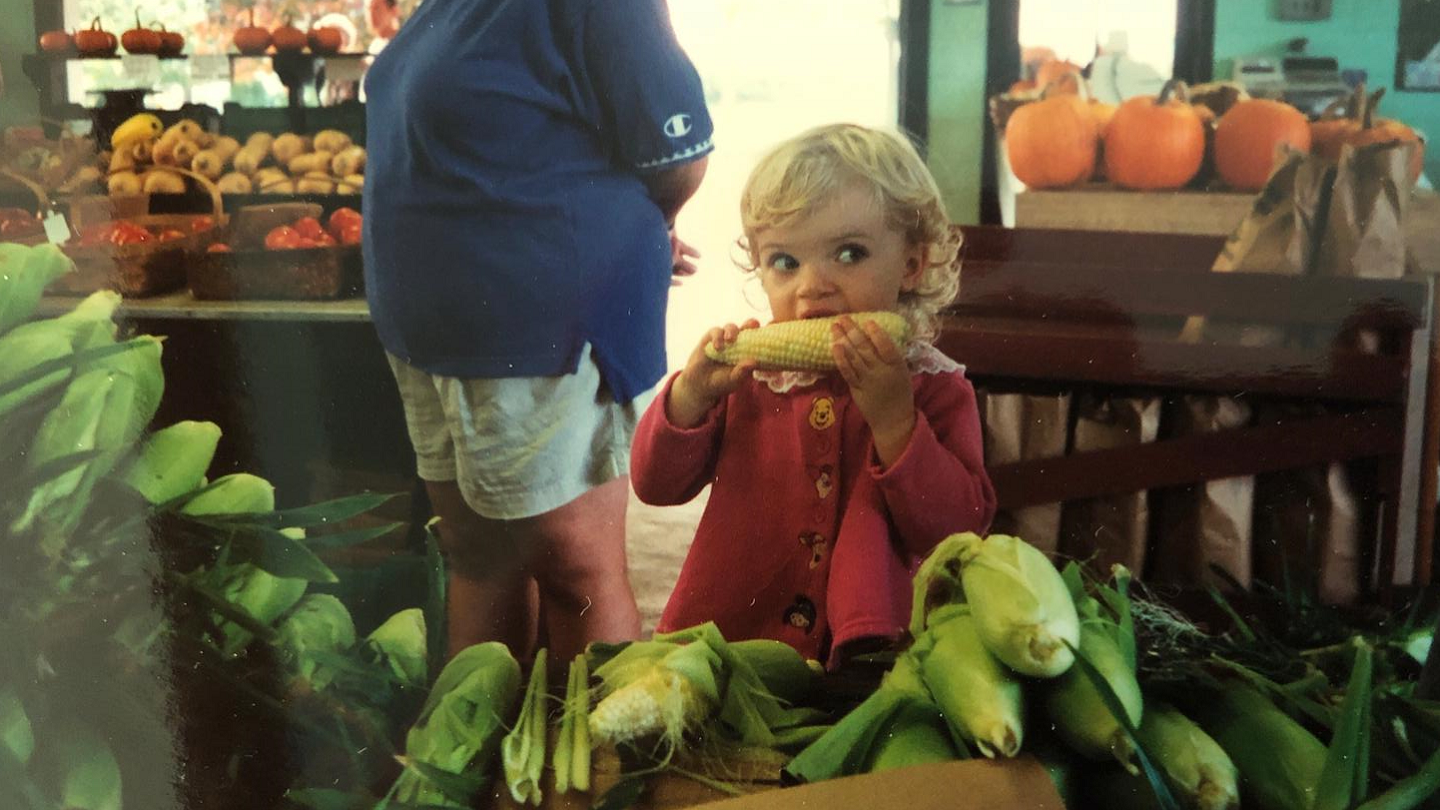 A little girl takes a bite out of an ear of corn inside a US farmstand