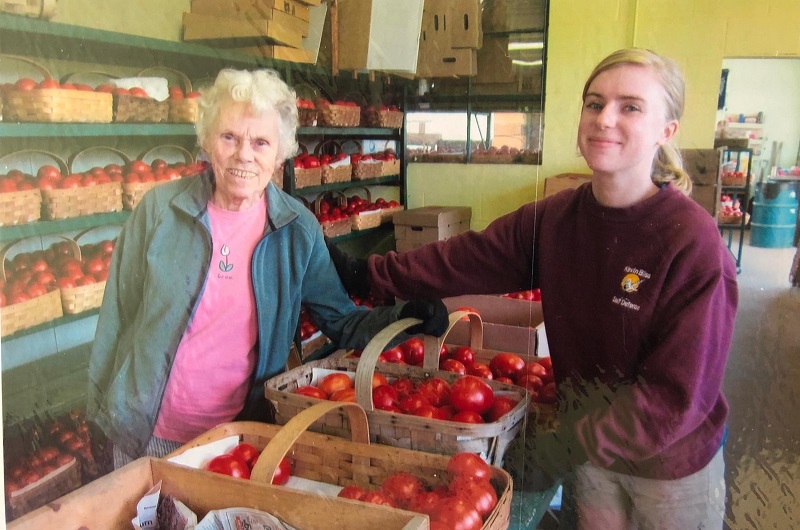 A young woman and an older woman with baskets of ripe tomatoes.