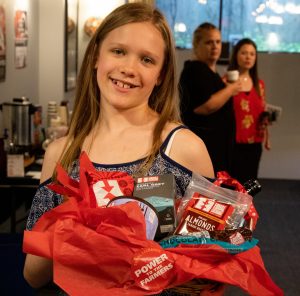a young girl holds a gift basket full of fair trade goodies like almonds, tea, and coffee with a sticker that says "power to the farmers".