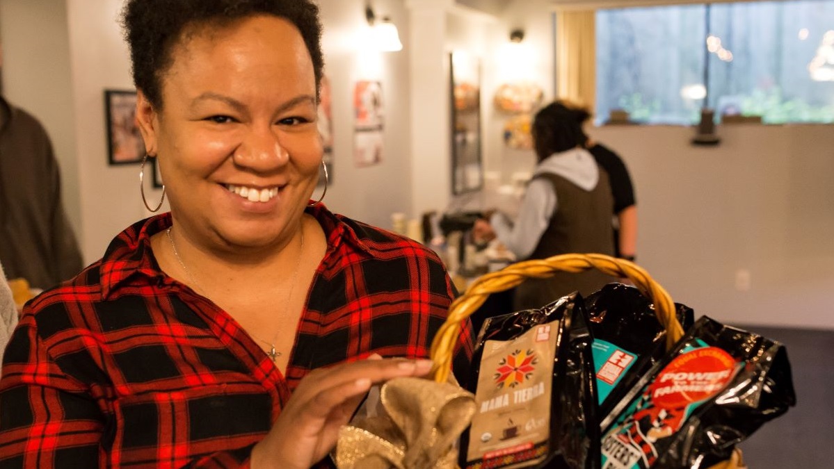 A smiling woman holds a gift basket of 3 fair trade coffees