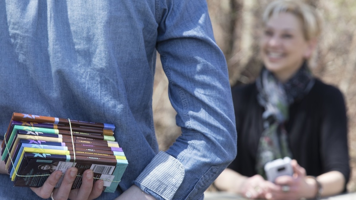 A woman surprises another woman with a stack of fair trade chocolate bars