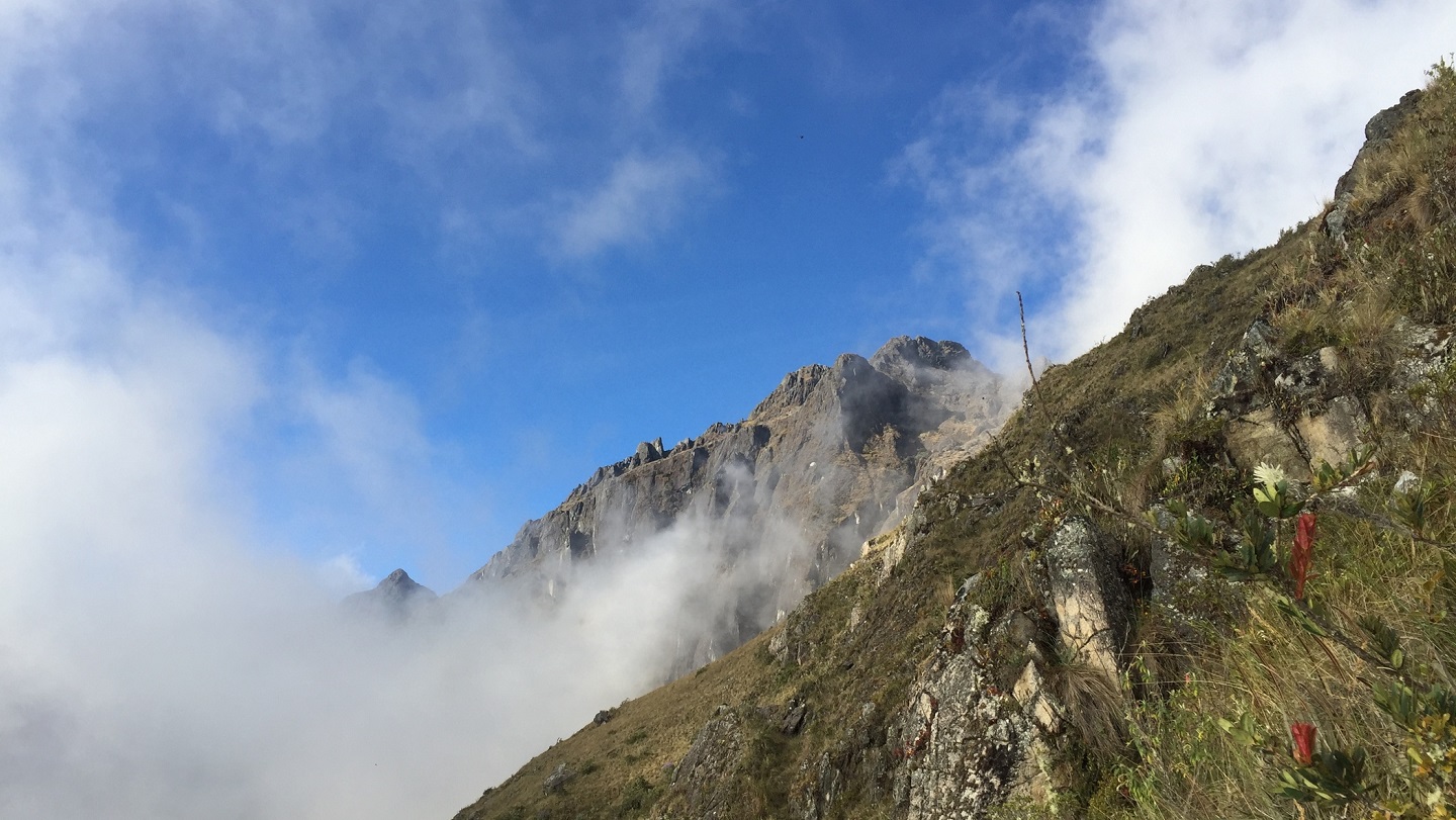 A craggy mountain in Peru in front of a blue sky with wisps of cloud