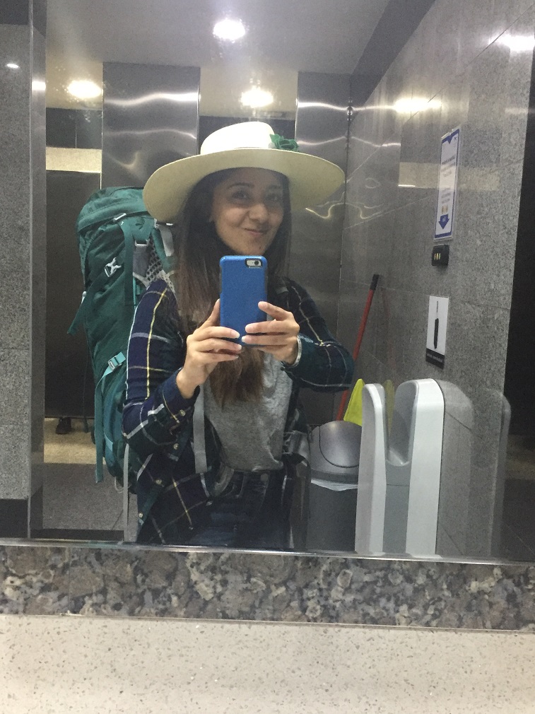 A woman wearing a backpack smiles at herself in the mirror
