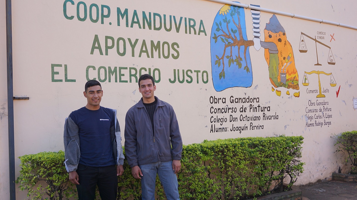 Two men stand in front of a mural at the Manduvira co-op in Paraguay