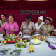 Group of women cooks at a table full of bananas and cakes, under a sign reading 'Bienvenidos'